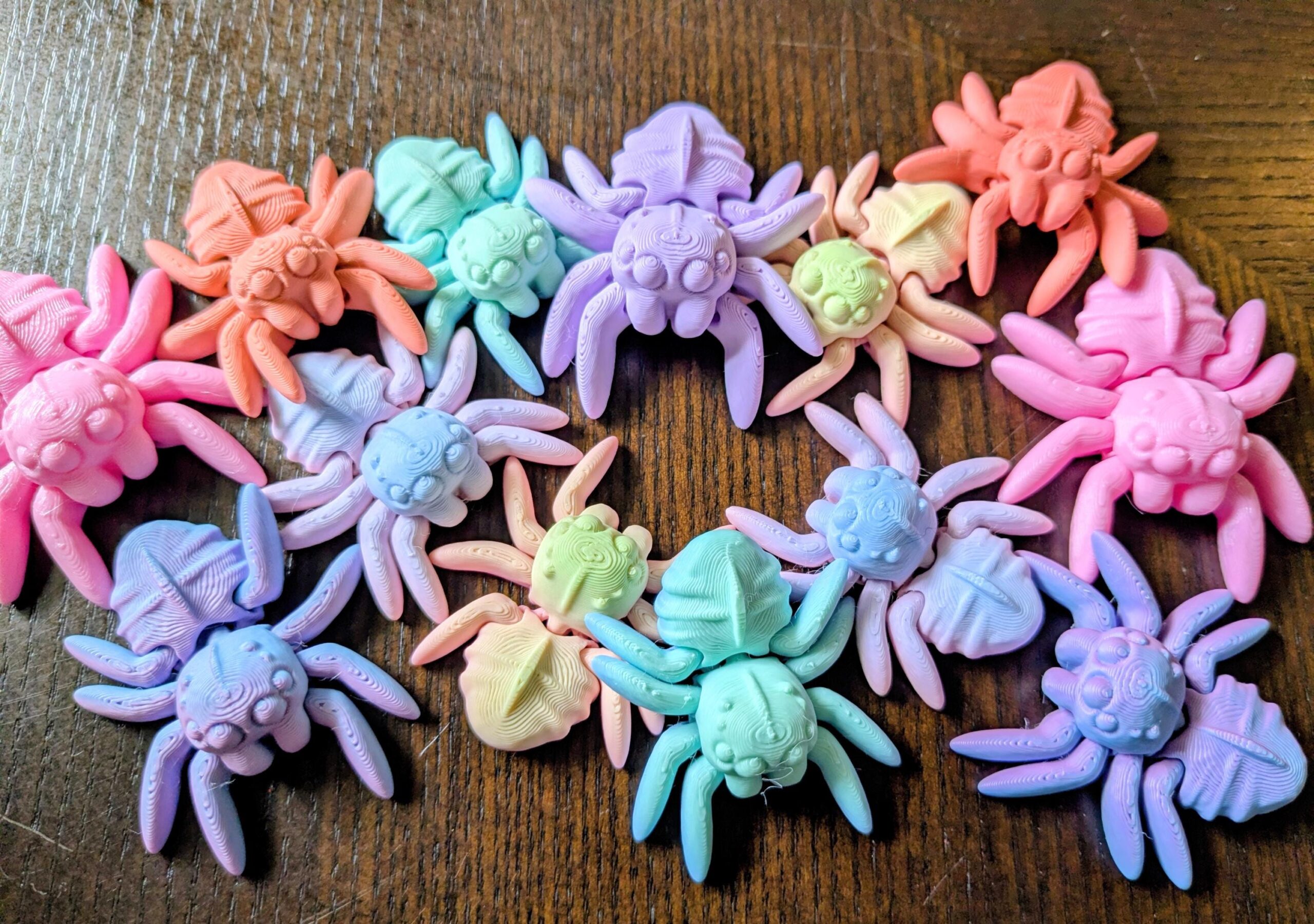 May include: A collection of colorful, 3D-printed spider figurines in various pastel shades, including pink, orange, blue, green, and purple. The spiders have detailed body and leg features, perfect for decorative purposes.