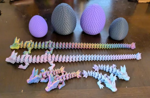 May include: A collection of 3D-printed dragon toys and textured eggs in various sizes and colors. The dragons are articulated and multi-colored, while the eggs are purple and gray.