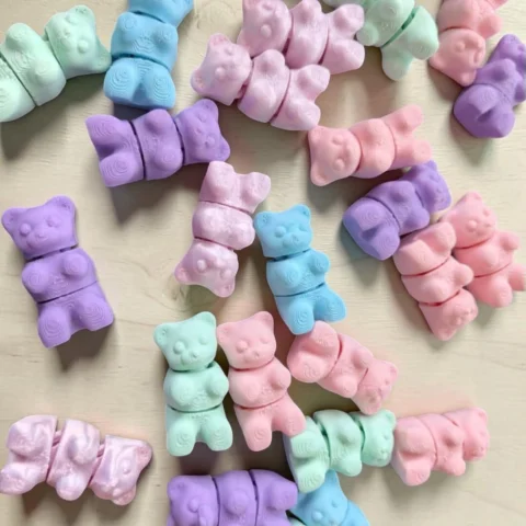 May include: A collection of small, three-dimensional bear-shaped figures in pastel shades of mint green, light blue, lavender, and soft pink. Each bear figure features a smooth, matte surface with molded facial details and rounded limbs.