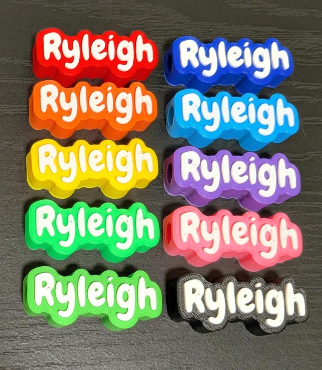 May include: Ten rectangular silicone beads arranged in two columns, each featuring the name Ryleigh in white raised lettering. The beads come in a variety of solid colors including red, orange, yellow, green, light green, blue, cyan, purple, pink, and black.