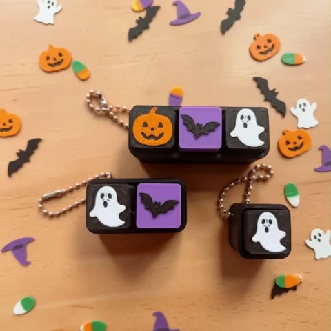 May include: Three black mechanical keyboard keycap keychains with Halloween motifs. One features an orange pumpkin, a purple bat, and a white ghost. Another has a white ghost and a purple bat. The third is a single keycap with a white ghost.