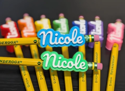 May include: A collection of yellow Dixon Ticonderoga HB number 2 pencils, each topped with a custom 3D-printed name topper. The toppers feature the name Nicole in white script lettering against various colored backgrounds including blue, green, red, orange, yellow, purple, and pink.