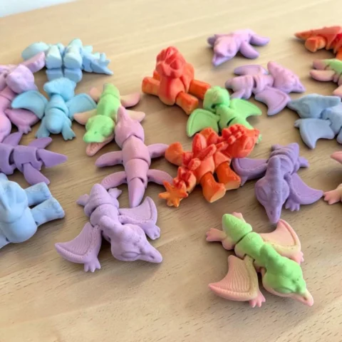 May include: A collection of small, molded dinosaur-shaped erasers in various pastel and bright colors including light blue, lavender, lime green, and orange. Each eraser features articulated segments and detailed wing or limb structures.